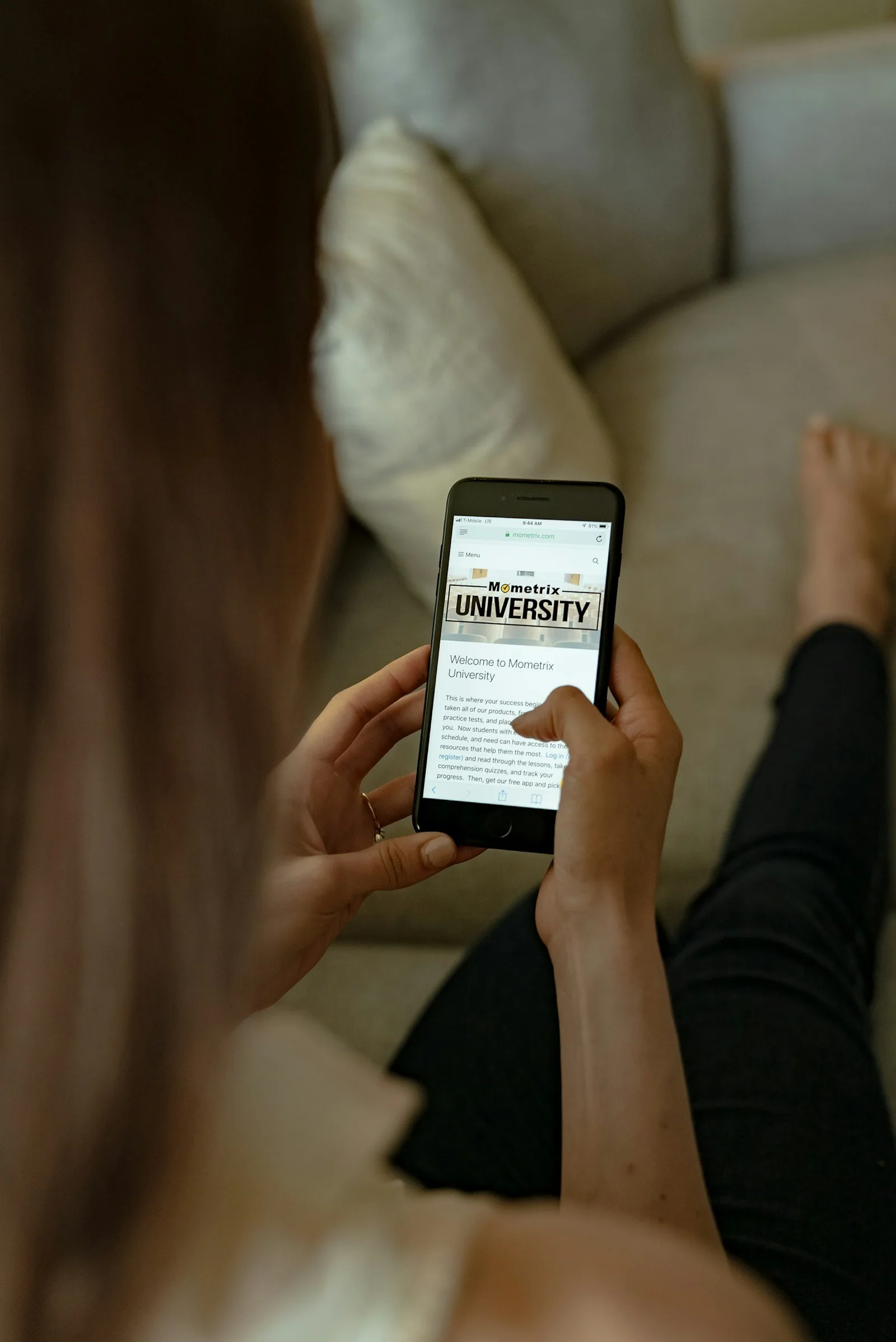 A person reviewing study material on a smartphone while seated on a sofa